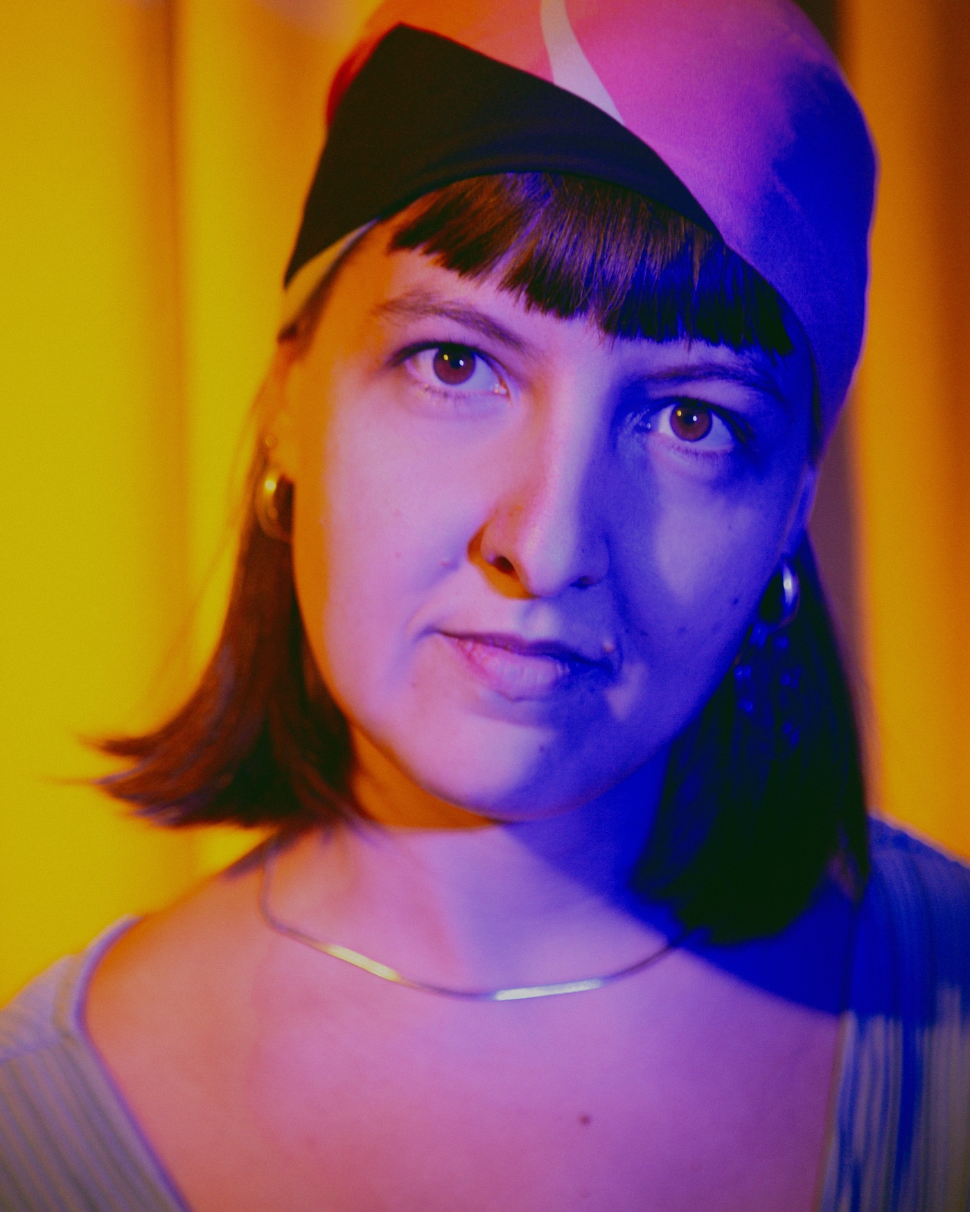 Die junge Frau blickt forschend in die Kamera, farbig ausgeleuchtet.