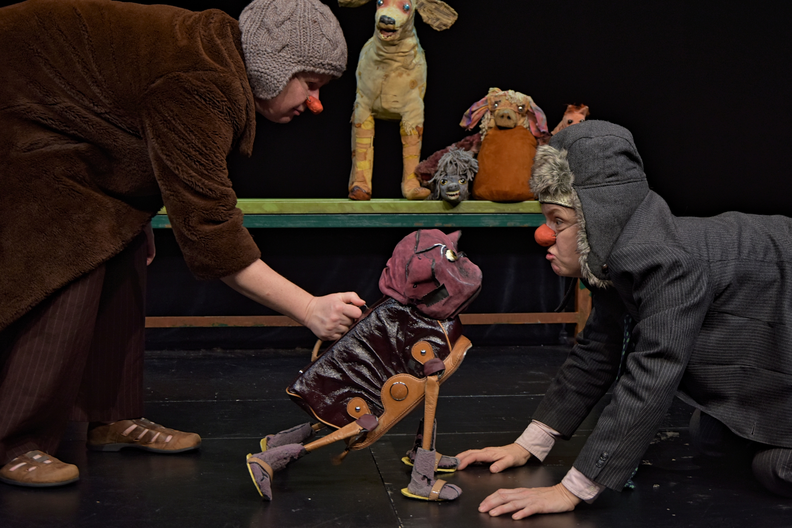 Ein Mensch mit Clownsnase auf allen Vieren vor einer Hundepuppe.