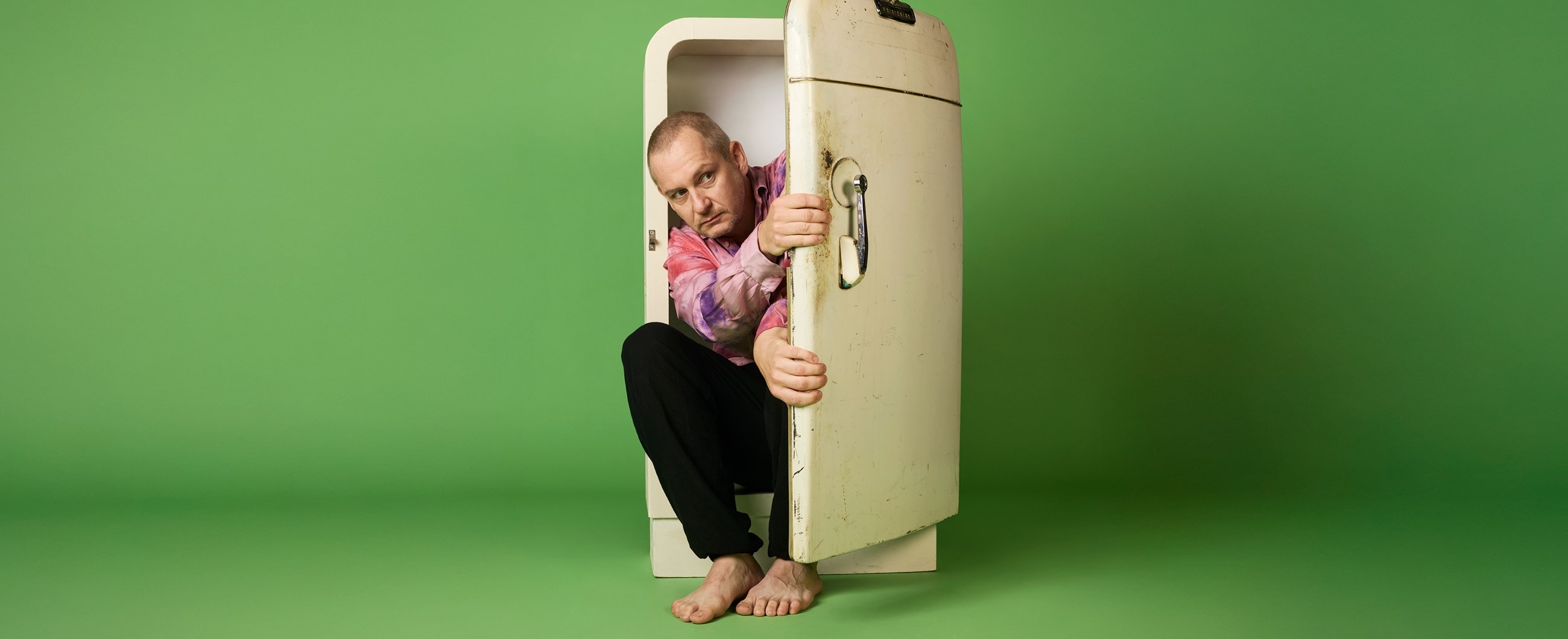 Mann sitzt in einem Kühlschrank und blickt zurückhaltend raus.